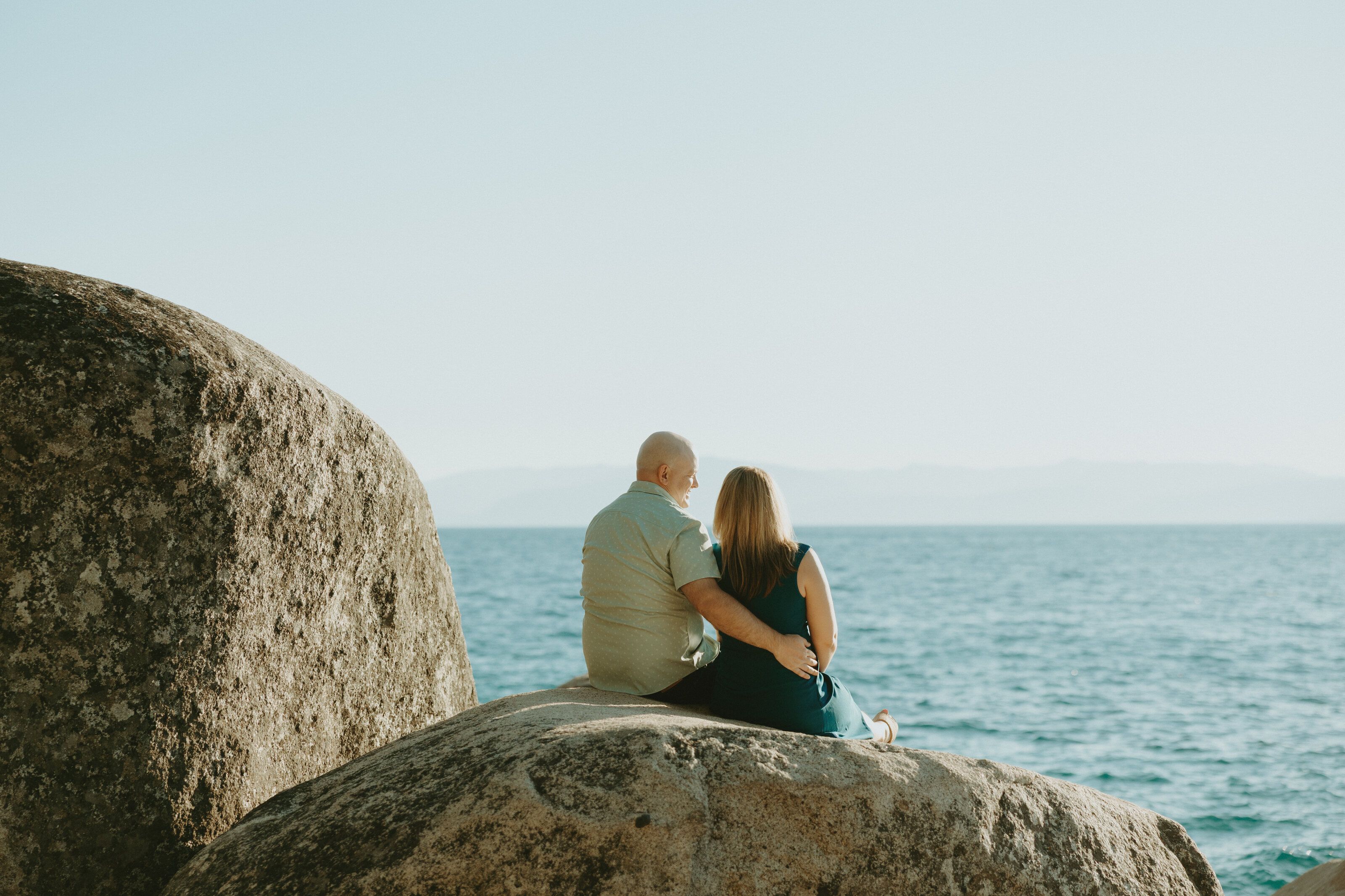 Nicole and Eric sitting together on a granite boulder, gazing out over Lake Tahoe