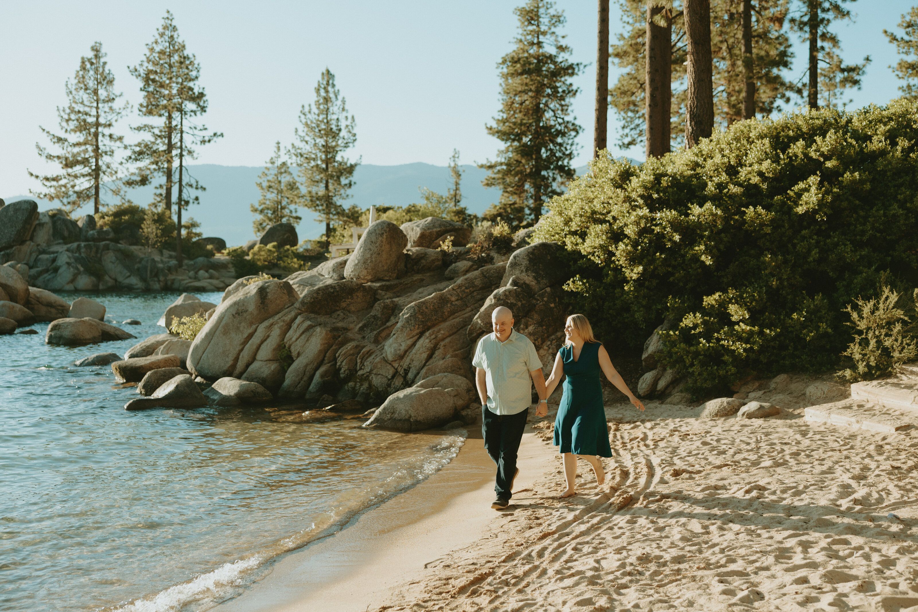 Nicole and Eric walking hand in hand along the Sand Harbor shoreline at golden hour